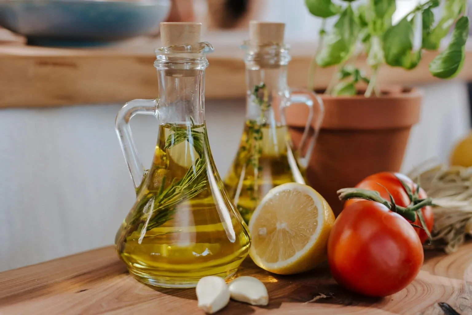 Glass bottles of olive oil with rosemary, a lemon half, tomatoes and garlic