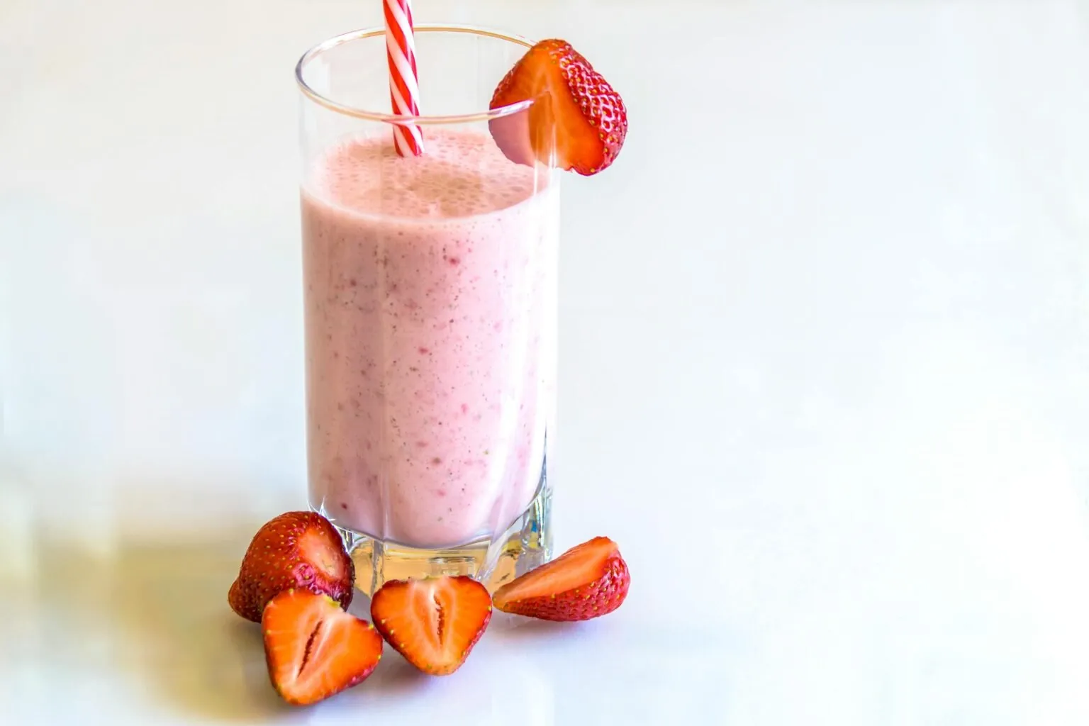 Strawberry smoothie in a tall glass with a striped straw and sliced strawberries