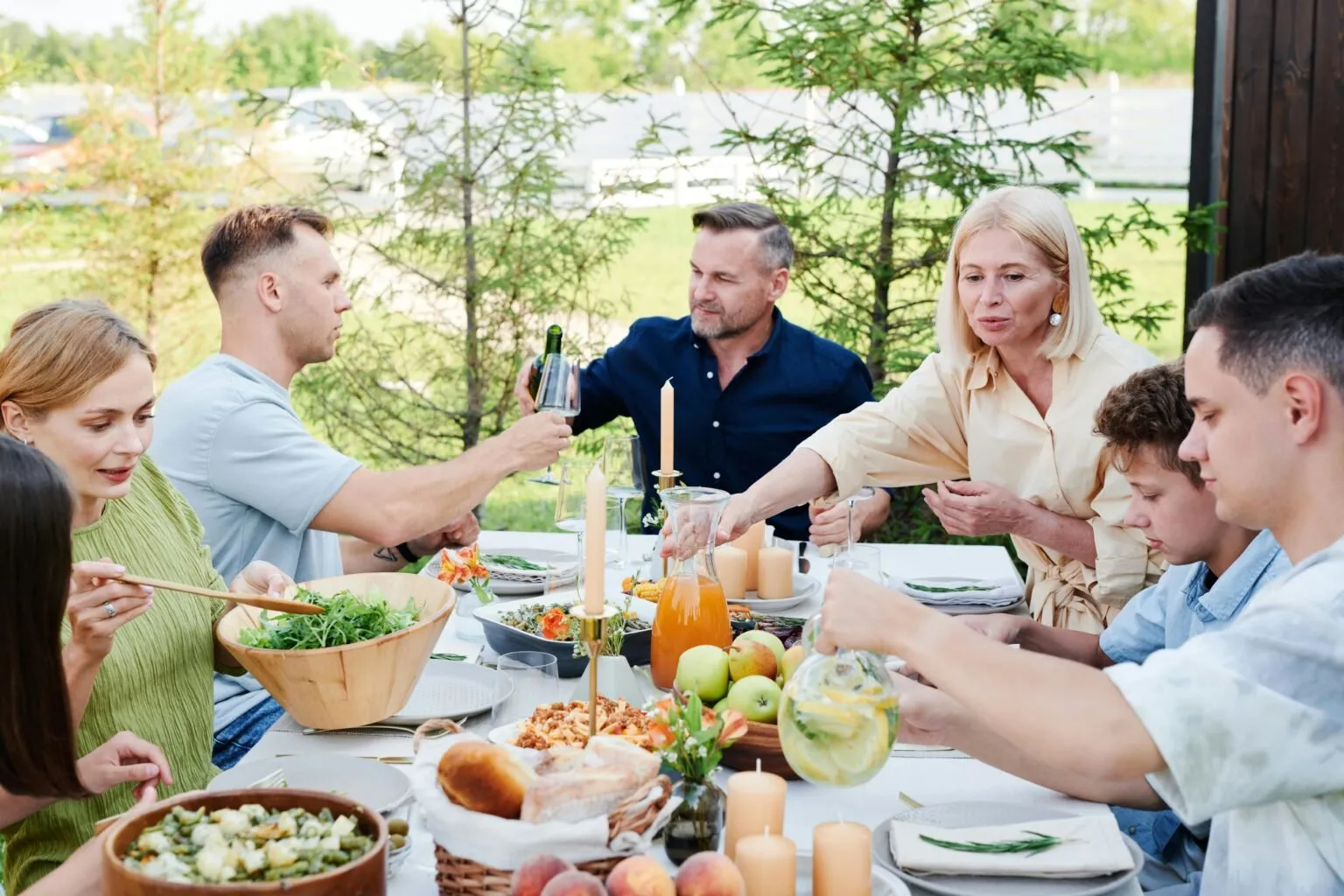 Family sharing an outdoor meal at a long table with salads, bread and fruit