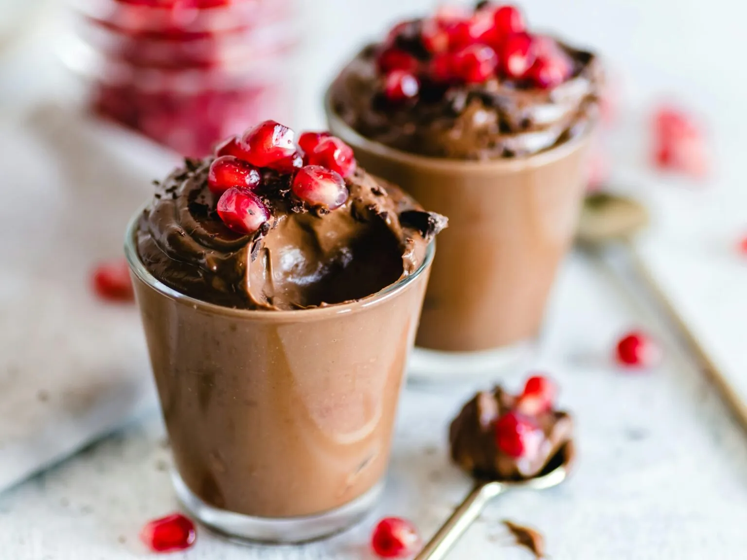 Two glasses of chocolate mousse topped with pomegranate seeds