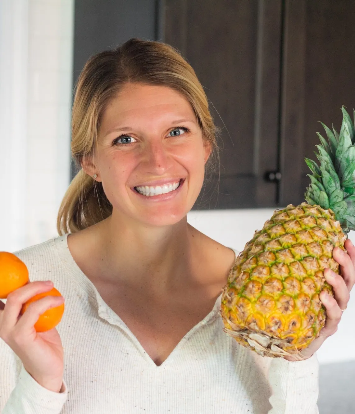 Kelsey Shaughnessy, RDN, smiling and holding oranges and a pineapple in a kitchen