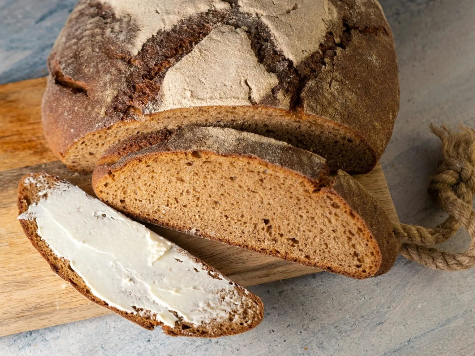 Loaf of whole grain rye bread with a buttered slice on a wooden board