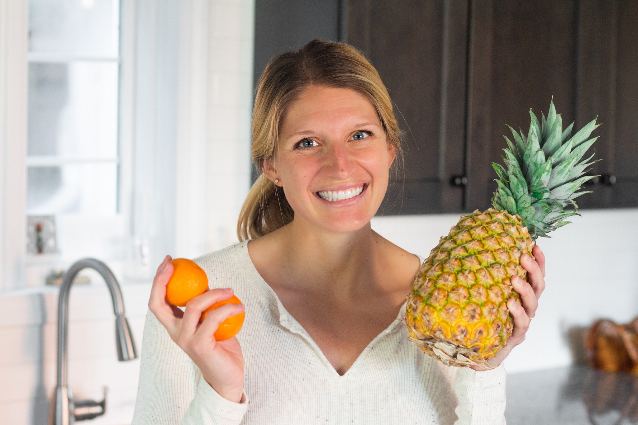 Dietitian Kelsey Shaughnessy holding oranges and pineapple in kitchen